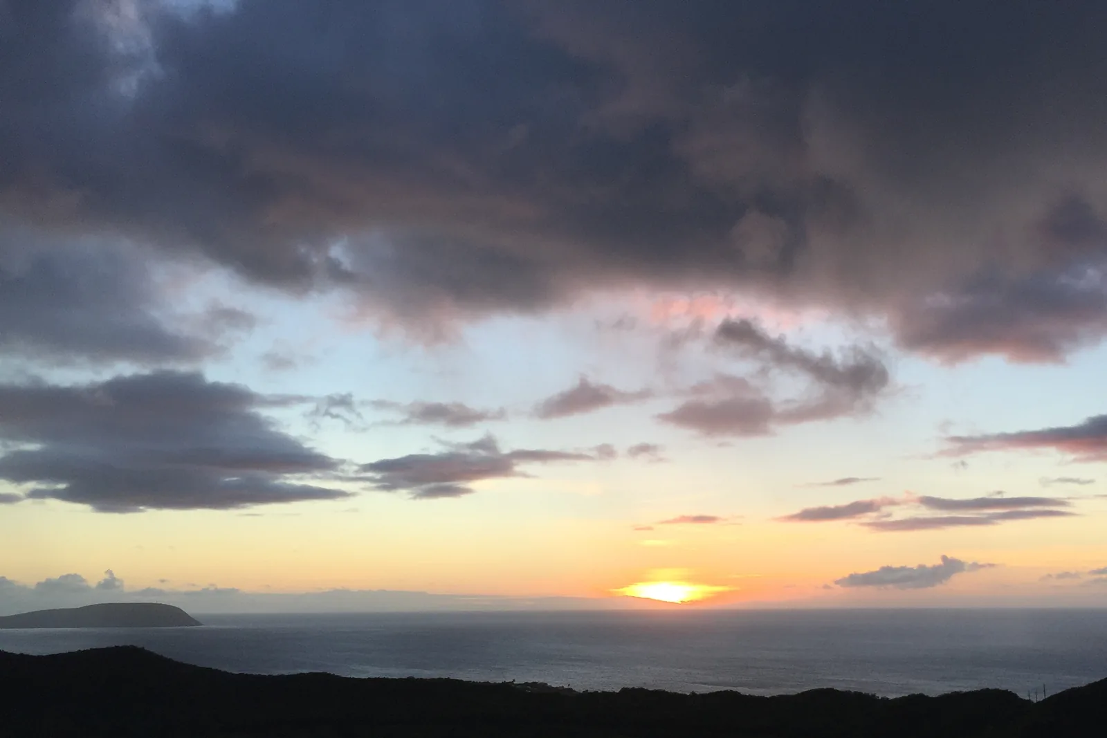 ダイヤモンドヘッドの頂上から見た日の出。雲の下の水平線に太陽が出ていて、左の奥に岬が見える